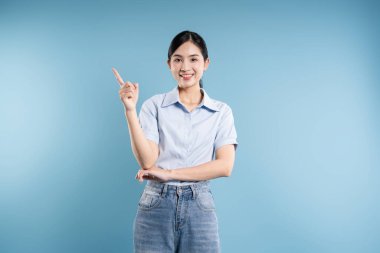 Koyu saçlı gülümseyen Asyalı bir kadın yukarı doğru bakan mavi bir arka planın önünde duruyor.