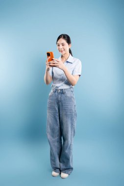 Düğmeli tişörtlü ve kot pantolonlu bir kadının mavi arka planda mobil bir cihazla etkileşime girdiği tam kare.