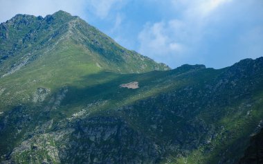 A flock of sheep grazing on a high altitude pasture on top of the sharp, rocky mountain peaks in Retezat mountains, Carpathia, Romania. Clouds are casting their shadow above the crest. 