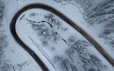 Aerial panorama of a winding gravel road winding along the snowed coniferous forests of Parang Mountains