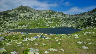 A campsite near Bucura lake at a high altitude in Retezat national Park. Alpine landscape. Carpathian Mountains, Romania. Lots of hiker tents are around the lake.