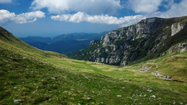 Panorama of Ialomita Valley in an alpine pasture. The valley is bordered by the vertical stone walls of Bucegi Mountains. Carpathia, Romania.