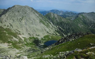 View from on top of Peleaga peak to a glacier lagoon next to another rocky mountain summit. Alpine landscape in Retezat Mountains, Carpathia, Romania.