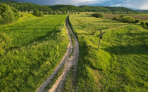 Railway level crossing with a Saint Andrew's Cross sign. Old railroad crossing a plain field near a forested hill. Countryside landscape, Romania. Sunset