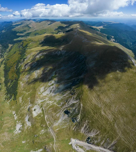 Aerial drone panorama above the Parang mountains massif. The alpine grasslands are shaded by clouds. Sky is blue at the horizon. Carpathia, Romania