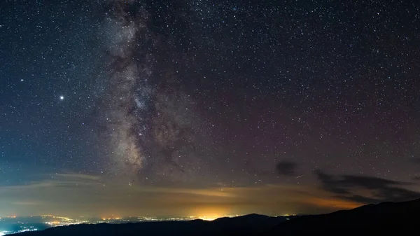 Milky way seen seen from the mountains, rising above urban city polution in a summer night. Astrophotography with stars and constellations.