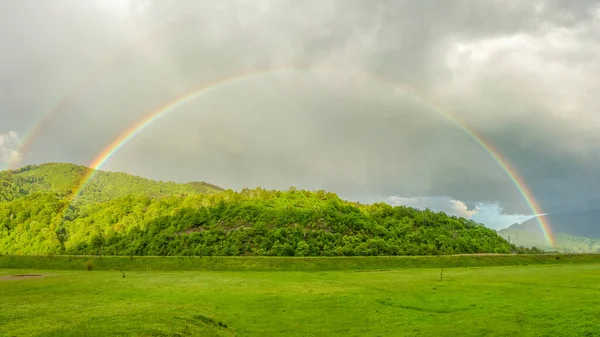 彩虹在雨天出现在农村地区上方的拱形彩色彩虹森林被五彩斑斓的现象和透过云彩出现的阳光照亮了 罗马尼亚喀尔巴阡山 — 图库照片