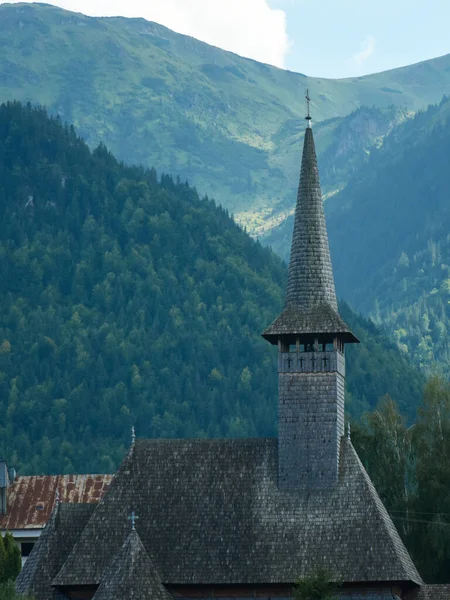Eski ahşap, ortodoks Hıristiyan kilisesinin çan kulesi çatısı tamamen ahşaptan yapılmıştır. Arka planda bir dağ sırtı ve ormanlar var. Carpathia, Romanya.