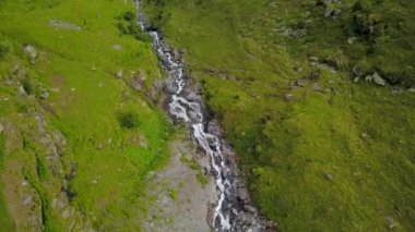 Yokuş aşağı akan hızlı bir nehrin üzerinde uçarken bir dağ sırtı, çimenli otlaklar boyunca. Fagaras Dağları 'ndaki yüksek irtifa manzarası. Carpathia, Romanya.