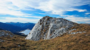 Vidra Gölü, mavi gökyüzünü gösteren keskin nasırlı bir uçurumun arkasında saklanıyor. Latorita Dağları 'na sonbahar geldi. Kurumuş alp otlaklarının üzerine turuncu rengini getirdi. Karpatya.