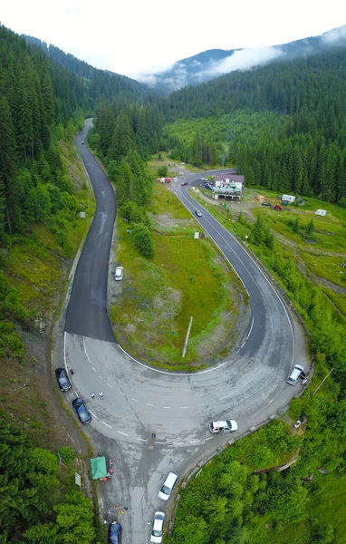 Aerial drone view of a crossroad. The road is located in a mountainous area, and crosses dense spruce forests. Cloudy and foggy summer day. Carpathia, Romania