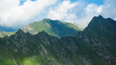 Romanya 'nın Carpathia kentindeki yeşil dağlarla kaplı Fagaras dağlarındaki keskin, kayalık dağ zirveleri. Aşınmış sivri tepeler gölge ve bulutlarla kaplıdır.. 