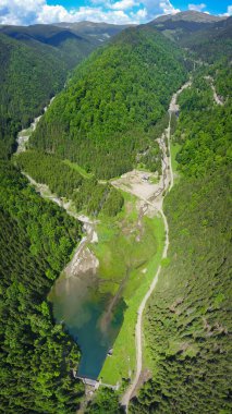 Balota Gölü ve Capatanii Massif 'in üzerinde yüksek irtifa zirveleri ve vahşi kozalaklı ormanlarıyla hava aracı görüntüsü. Bahar zamanı, Carpathia, Romanya. Göl suları mavi..