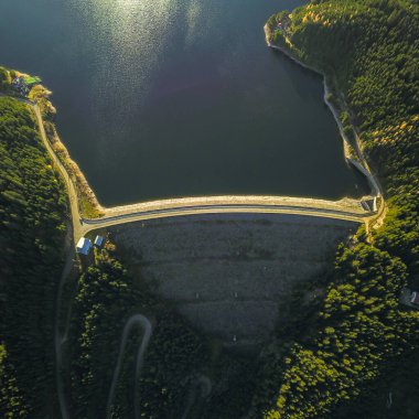 Gün batımında Vidra Gölü üzerinde dikey hava manzarası. Kayalardan yapılmış kemerli bir baraj suyu tutar. Baraj, Lotru Vadisi ve Dağları 'nın vahşi doğası içinde inşa edilmiştir. Carpathia, Romanya.
