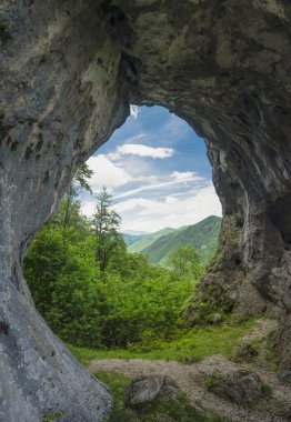 Dağlık bir ormanın tepesine ve bir mağaranın içindeki dağlara bakan dağ yamacındaki nasırlı bir uçurumda aşınmış bir manzara. Tünelin yosun ve yosunla kaplı taş duvarları var. Doğal fenomen.