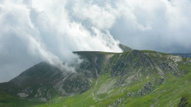 Fırtınalı bulutlar Parang dağlarının keskin tepelerini kaplıyor. Yaz mevsimi, dağlık çayırlar parlak yeşildir. Yağmur yağacak. Carpathia, Romanya.