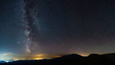 Dağlardan görülebilen Samanyolu, bir yaz gecesinde şehir kirliliğinin üzerinde yükseliyor. Ufuk turuncu renkte yanar. Yıldızlı ve takımyıldızlı astrofotoğrafçılık. Samanyolu 'nun çekirdeği yukarıda..