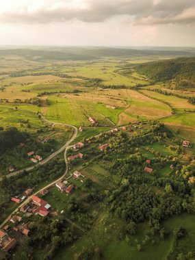 Günbatımında Transilvanya 'nın kırsal bir bölgesinin üzerinde insansız hava aracı uçuşu. Otlak tepeler, meyve bahçeleri, tarımsal alanlar, çayırlar, fırtına bulutları ve güneş ışığı güzel bir kırsal alan yaratır. Romanya
