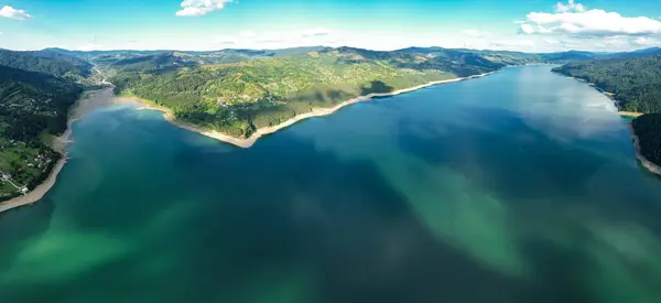Aerial drone panorama above Izvorul Muntelui Lake. Sunt is about to set. The blue waters are washing the shores of the nearby villages and tourists resorts. Ceahlau Mountains, Carpathia.