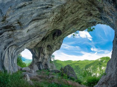 Dağların tepesindeki bir mağara manzarası, dağ yamacındaki nasırlı bir uçurumda aşınmış. Tünelin yosunlarla kaplı taş duvarları var. Mağaradaki kemerler bir sütun tarafından çözülmüş. Karpatya
