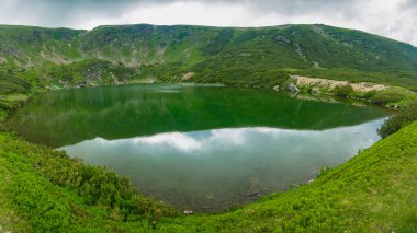 Cindrel Dağları 'nda bulunan bir buzul gölü. Dağların tepelerinde bulutların olduğu yağmurlu bir gün. Dağ çamları dağların kayalık tepelerinde yetişir. Carpathia, Romanya