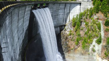 Bahar zamanı Galbenu barajı. Su barajı taşırıyor ve kemerli beton yapının üzerine dökülen şelaleyi oluşturuyor. Sürdürülebilir, hidroelektrik, enerji. Carpathia, Romanya.