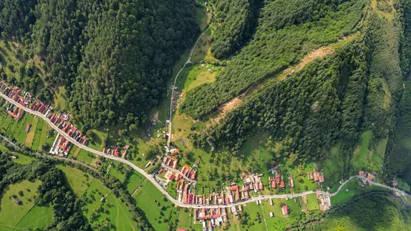 Nehir boyunca dağlık bir bölgede bulunan bir köyün üstündeki insansız hava aracı panoraması. Nehir ve yol kayın ormanlarının ve çayırların yanında esiyor. Kırsal alan, Carpathia, Romanya.