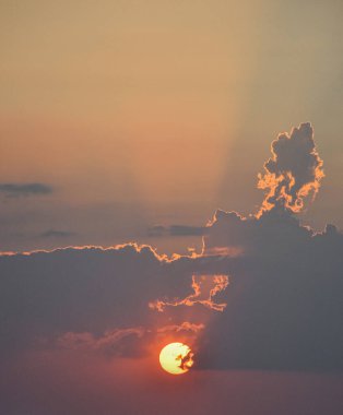 Parlak altın güneş alevli bulutların ardında batıyor, gökyüzü turuncudan maviye ve yumuşak gri tonlara canlı katmanlar halinde kayıyor.