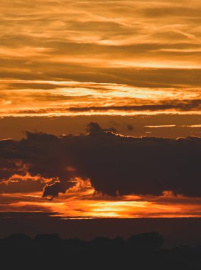 Şehir günbatımı, sıcak ve aydınlık gökyüzünü, aydınlık bulutları ve silikonlu bir şehir siluetini yakalar ve derinliği ve havasını yükseltir.