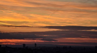 Şehir binaları dramatik bir günbatımı gökyüzünün altında altın ve turuncudan yumuşak mavi ve ılık griye dönüşüyor.