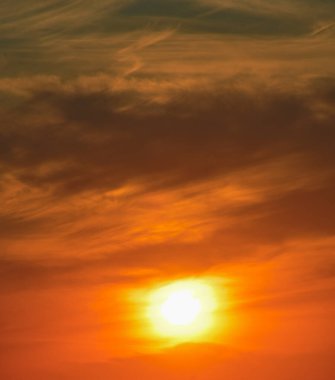 Canlı turuncu ve sarı gün batımı yumuşak, puslu bulutlar dramatik bir akşam gökyüzünde.