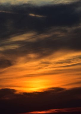 Canlı turuncu-sarı günbatımı rüya gibi bir gökyüzünde yumuşak gri bulutlara karışıyor..