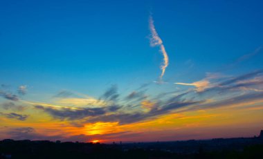 Yumuşak turuncu-gri bulutlu soyut gökyüzü ve alacakaranlıkta siluet içinde şehir silueti..