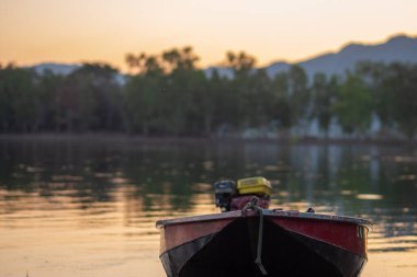 Huzurlu bir nehirde, altın günbatımının altında, huzurlu doğayı yansıtan bir tekne sürüklenir.