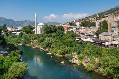 A picturesque scene of Neretva River peacefully flowing amidst a vibrant green hillside in Mostar, Bosnia and Herzegovina