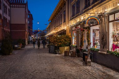 Göteborg, İsveç, Ocak 5, 2024. İnsanlar Haga Mahallesi 'nde tatil için dekore edilmiş büyüleyici binalarla dolu bir kaldırım taşı caddesi boyunca yürüyorlar.