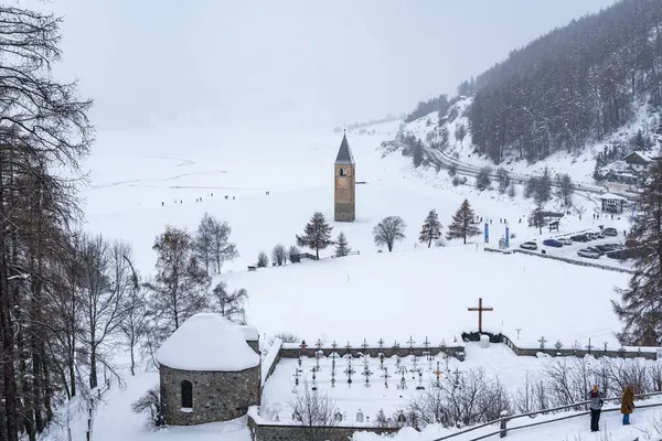 The bell tower stands prominently in the center of snow-covered Resia lake, surrounded by a serene winter landscape, Alto Adige, Italy