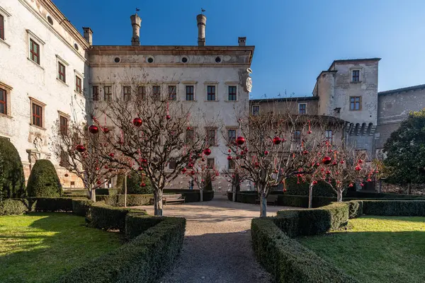A photograph showcasing the grand Buonconsiglio Castle with a meticulously landscaped garden in front of it, Trento, Italy