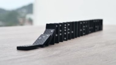 Domino effect in slow motion - falling black tiles with white dots. Dominoes falling in line effect business concept. High quality FullHD footage
