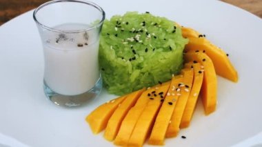 Pirinç lapalı beyaz tabak ve taze olgun tatlı mango üzerine susam tohumu serpiştirilmiş ve bir bardak pirinç sütü içilmiş.