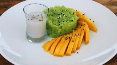 Pirinç lapalı beyaz tabak ve taze olgun tatlı mango üzerine susam tohumu serpiştirilmiş ve bir bardak pirinç sütü içilmiş.