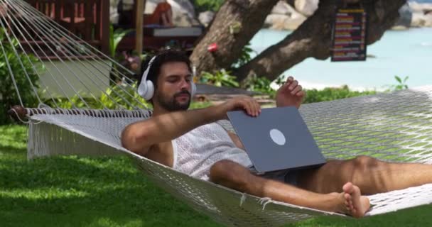 Kablosuz Kulaklıklı Beyaz Erkek Turist Dizüstünü Kapatıp Plaj Hamağında Yatıyor — Stok video
