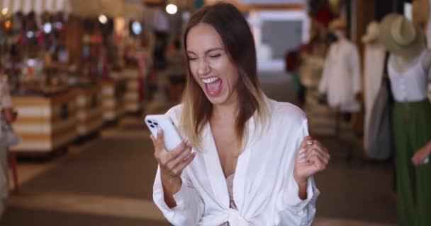 漂亮的女人在购物中心里用智能手机 滚动的新闻资料 紧紧抓住幸福和好消息的拳头 — 图库视频影像