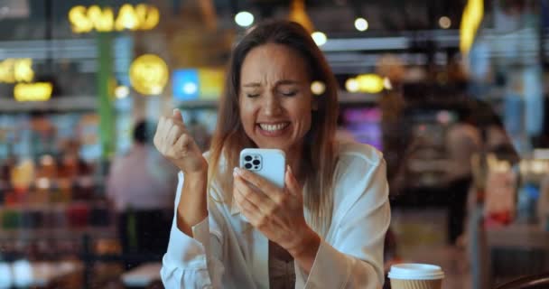 快乐的女商人喜欢在咖啡店办公室的智能手机上取得成功 令人惊讶的女士慢吞吞地在电话里看到好消息 — 图库视频影像