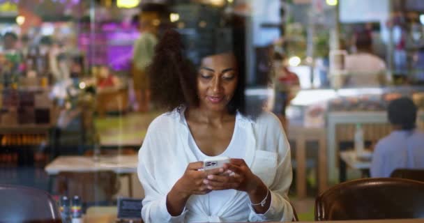 アフリカの民族の笑顔の女性 携帯電話を使用して コンテンツをチェック メッセージを書き込み コーヒーブレイク中にリラックス — ストック動画