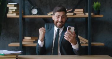 Şaşkın iş adamı kumarbaz kazanmakla ilgili iyi haberler alıyor. Heyecanlı erkek piyango talihlisi akıllı telefona bakarak başarıyı kutluyor, ofiste evet jestleri yapıyor. Mobil zafer kavramı
