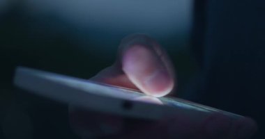 Genç adamın parmağı akıllı telefondaki parşömen uygulamalarına aktif olarak dokunuyor ve sosyal ağları tarıyor. Erkekler, akşam saatlerinde akıllı telefondan internet sayfalarına el yordamıyla bakıyorlar.