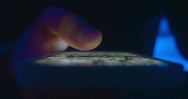 Yakından bir erkek, internet sosyal medya sayfalarını karıştırıyor. Akşamları akıllı telefondan internet sayfalarını çeviriyor. Erkek parmak kaydırma ekranı, akıllı telefon uygulaması ve gece sosyal ağları tarama