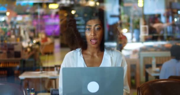アフリカ系アメリカ人の素敵な女性がオンラインビデオ通話を話しています カフェでテーブルに座り ノートパソコンを使い ビジネスパートナーやクライアントとビデオ通話でオンライン会議を行うことに成功しました — ストック動画