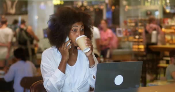 多任务积极的非洲裔美国女商人讲智能手机 在笔记本电脑上打字 喝着咖啡出去 在咖啡店工作 有信心的商界女性从自助餐厅进行电子通勤 — 图库视频影像